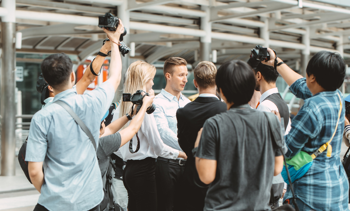 business man important press release surrounded scramble with reporters newspaper journalist photographer (c) AdobeStock