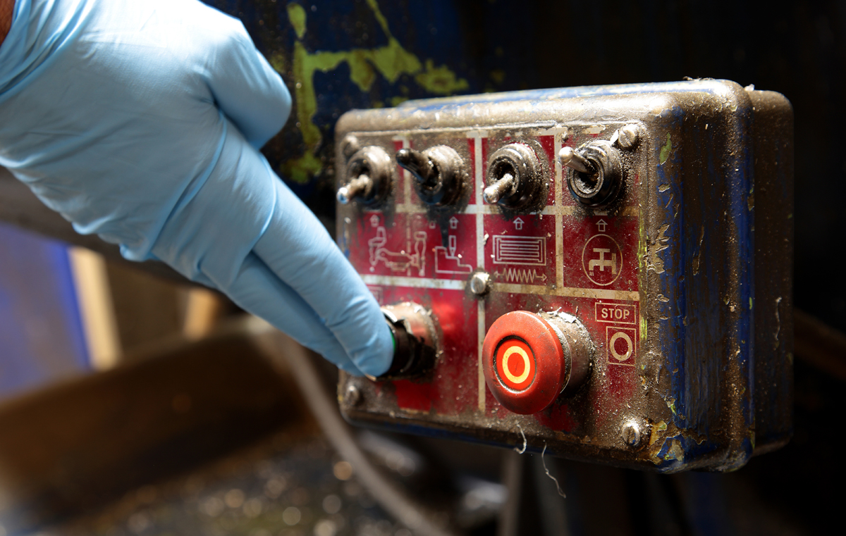 Man pressing button on an industrial machine control panel. (c) AdobeStock