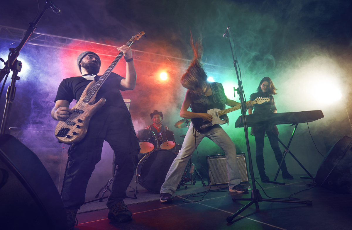 Rock band performs on stage. Guitarist, bass guitar and drums. Scene, light. (c) AdobeStock