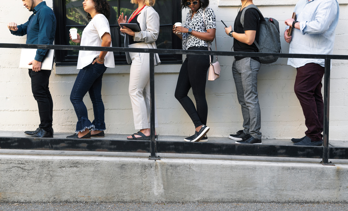 Business people holding digital devices while waiting in line. (c) AdobeStock