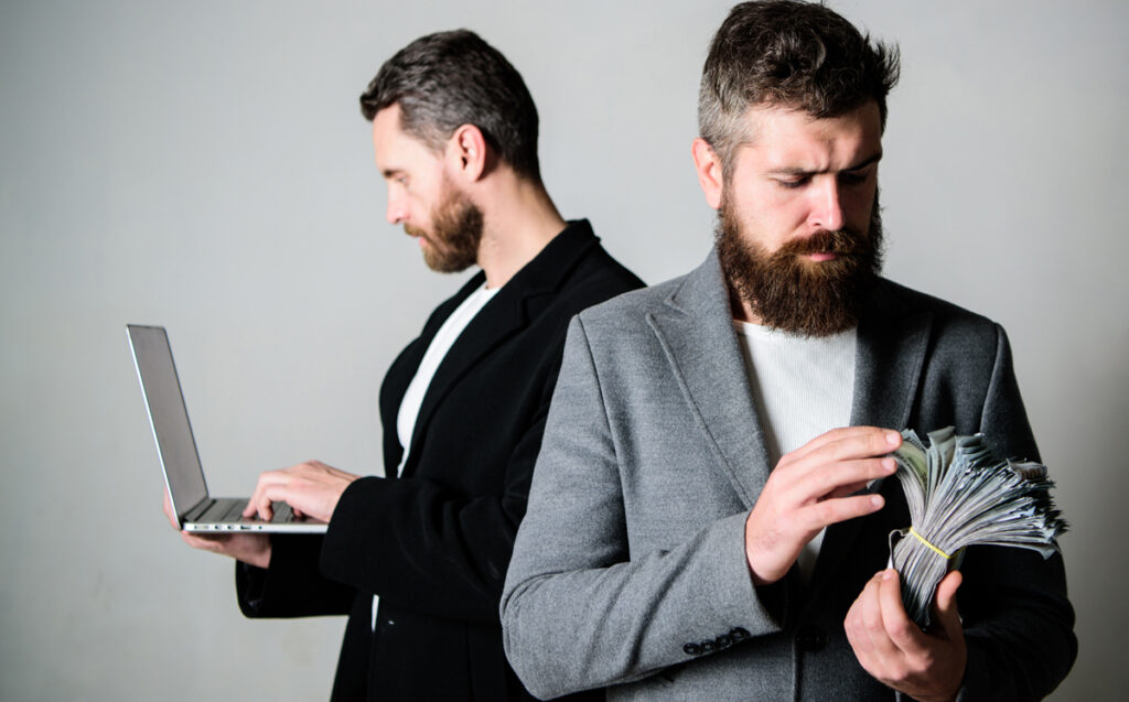 Ein Mann mit Laptop in der Hand beim Coden, davor ein anderer mit einem Bündel Geldscheinen, Stichwort End-User.
(c) AdobeStock