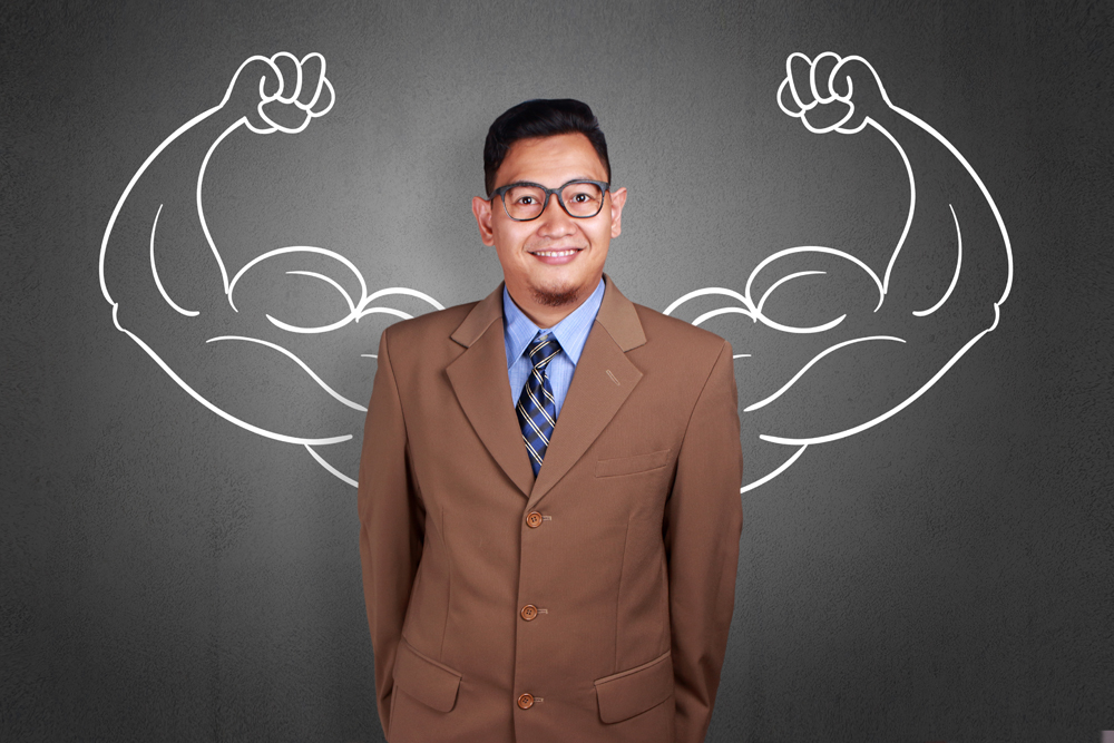 Business power concept. Young funny Asian businessman  smiling with strong powerful arms drawn behind. Inner power authority, Stichwort Mitarbeiter vs. Führungskraft.
(c) AdobeStock