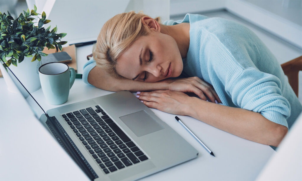 Eine vor einem Laptop am Schreibtisch schlafende Frau, Stichwort Servicechat.
(c) AdobeStock