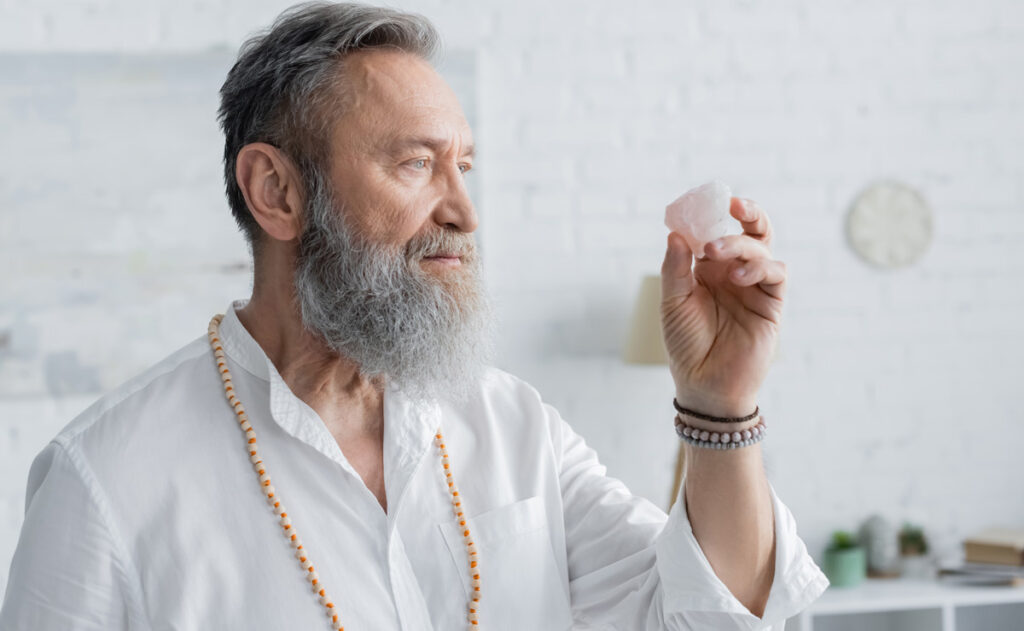 Ein "Guru" mit weißem Hemd und Vollbart beim Betrachten eines weißen Steins, Stichwort Kult.
(c) AdobeStock