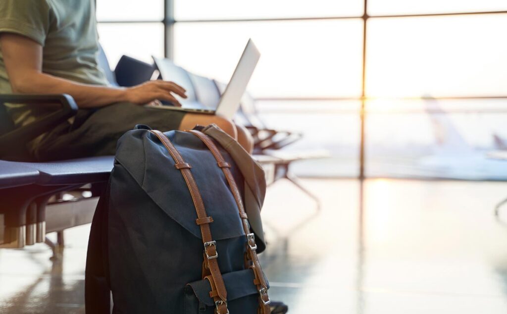 Ein Mann mit Laptop im Wartebereich eines Flughafens, Stichwort Mietpreise.
(c) AdobeStock