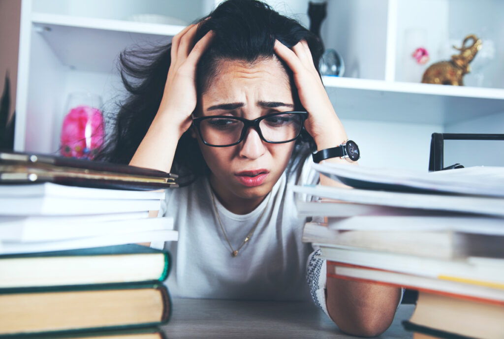 Eine müde Studentin hinter einem Berg von Büchern, Stichwort Netflixabo.
(c) AdobeStock