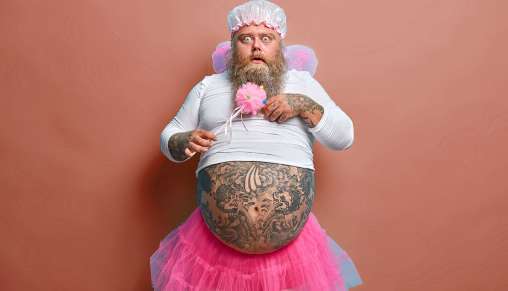 Ein Mann mit Vollbart und zahlreichen Tattoos in rosa-weißem Babygewand, Stichwort Social-Media-Regel.
(c) AdobeStock