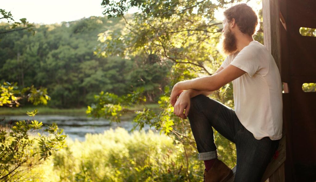 Ein Mann mit Vollbart schaut auf einen idyllischen See, Stichwort letzte Generation.
(c) AdobeStock