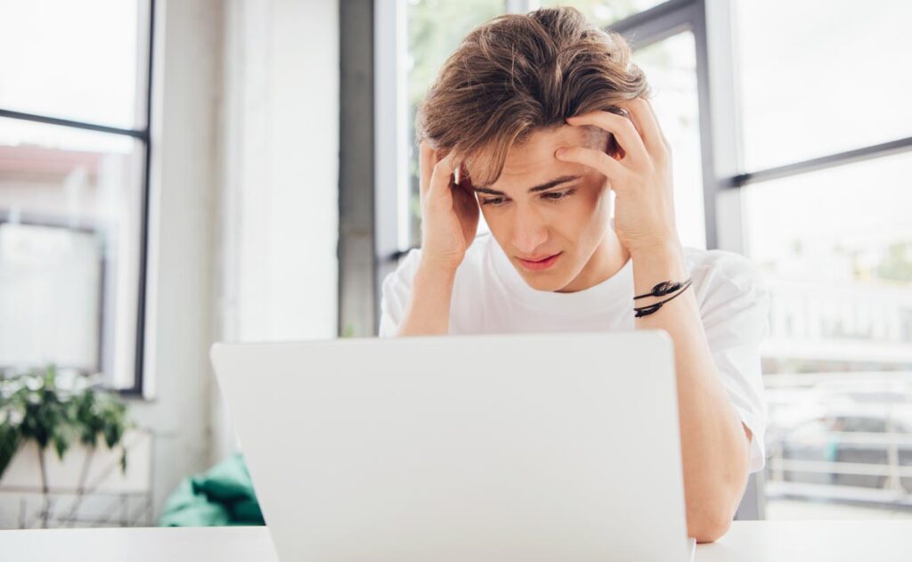 Ein junger Mann blickt, sich die Haare raufend, verzweifelt auf einen Laptopmonitor, Stichwort betreutes Denken.
(c) AdobeStock