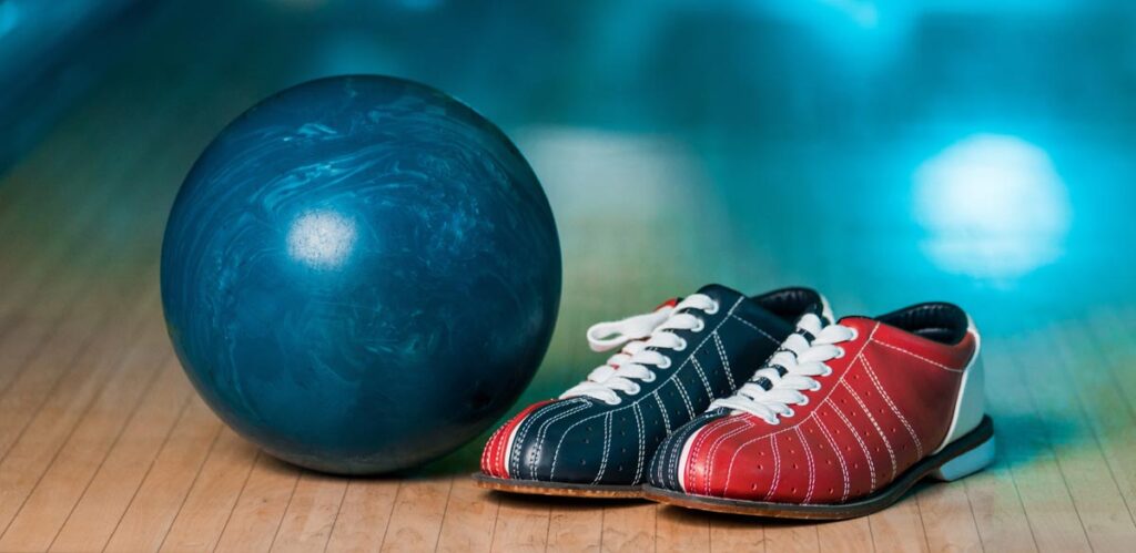 Kegelschuhe neben einer Bowlingkugel auf einer Kegelbahn, Stichwort Rapid.
(c) AdobeStock